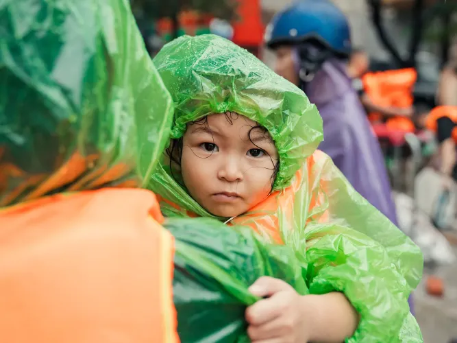 Little girl in raincoat is held by an adult. 