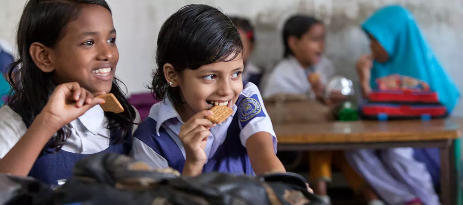 Two smiling schoolgirls of grade three enjoy protein-rich biscuits during their break period at Sher-E- Bangla Govenment Primary School, in Dhaka, Bangladesh, in October 2013.
