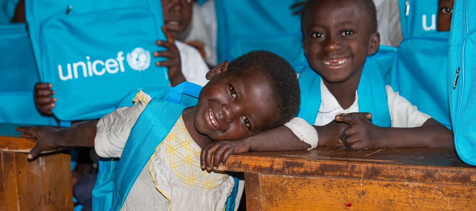 Children in a classroom with their blue backpacks with the UNICEF logo on. 