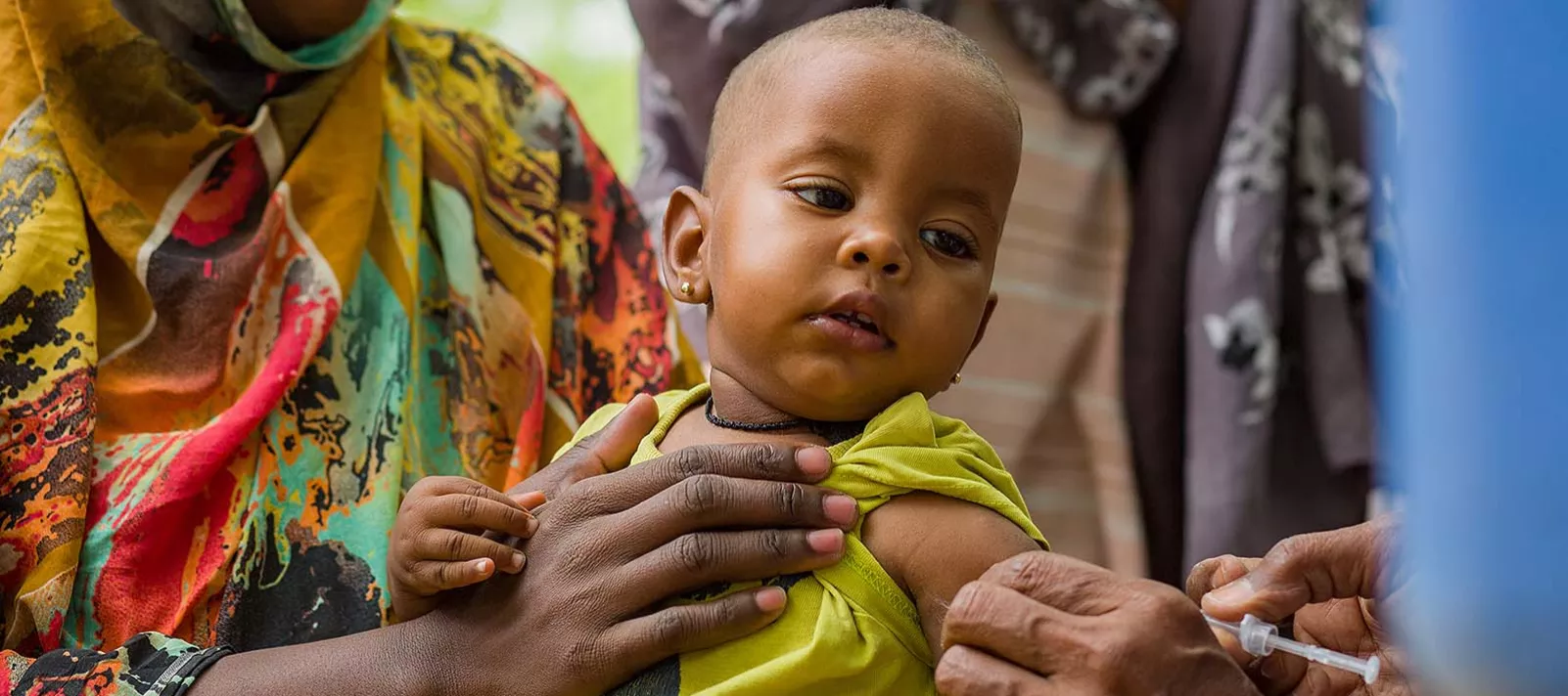 A baby is held by a woman while receiving a shot in her left arm.