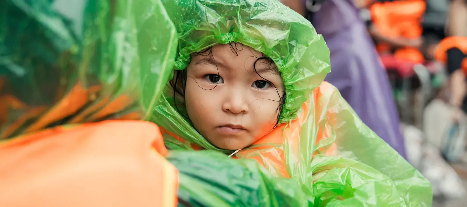 Little girl in raincoat is held by an adult. 