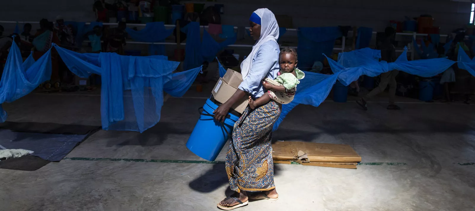 A woman living in Desportivo, a temporary accommodation centre in Pemba, Mozambique, walks carrying her baby in the pack and UNICEF hygiene kits containing clothes, underwear and sanitary products.