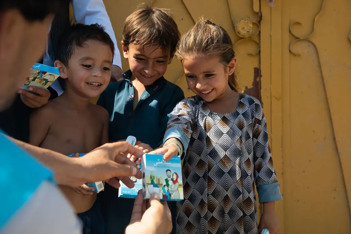 Three children smile while receiving ORS powders and soaps