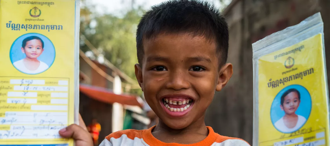 A smiling boy shows his and his siblings' vaccination cards, in Svay Pak Village, Phnom Penh, Cambodia, in March 2017. 