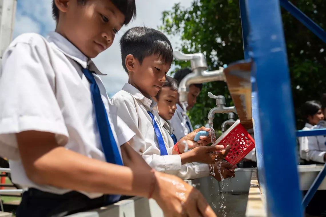 Boys wash their hands at an outdoor handwashing station.