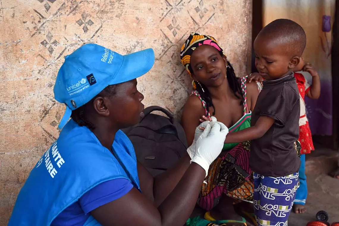 A young boy is tested by a healthcare worker wearing UNICEF-branded apparel while watched by a woman. 