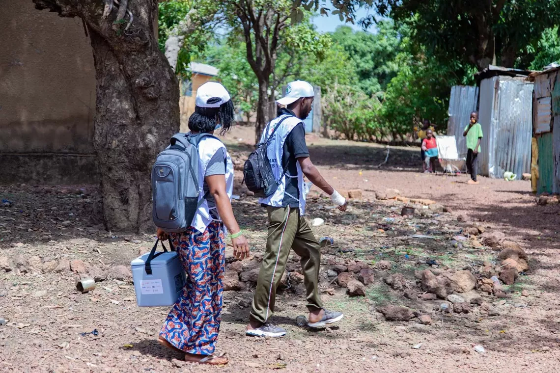 Two health workers bearing vaccine carriers walk through a neighbourhood in the community of Ley-Gnemb&eacute; in Lab&eacute;, Guinea. 