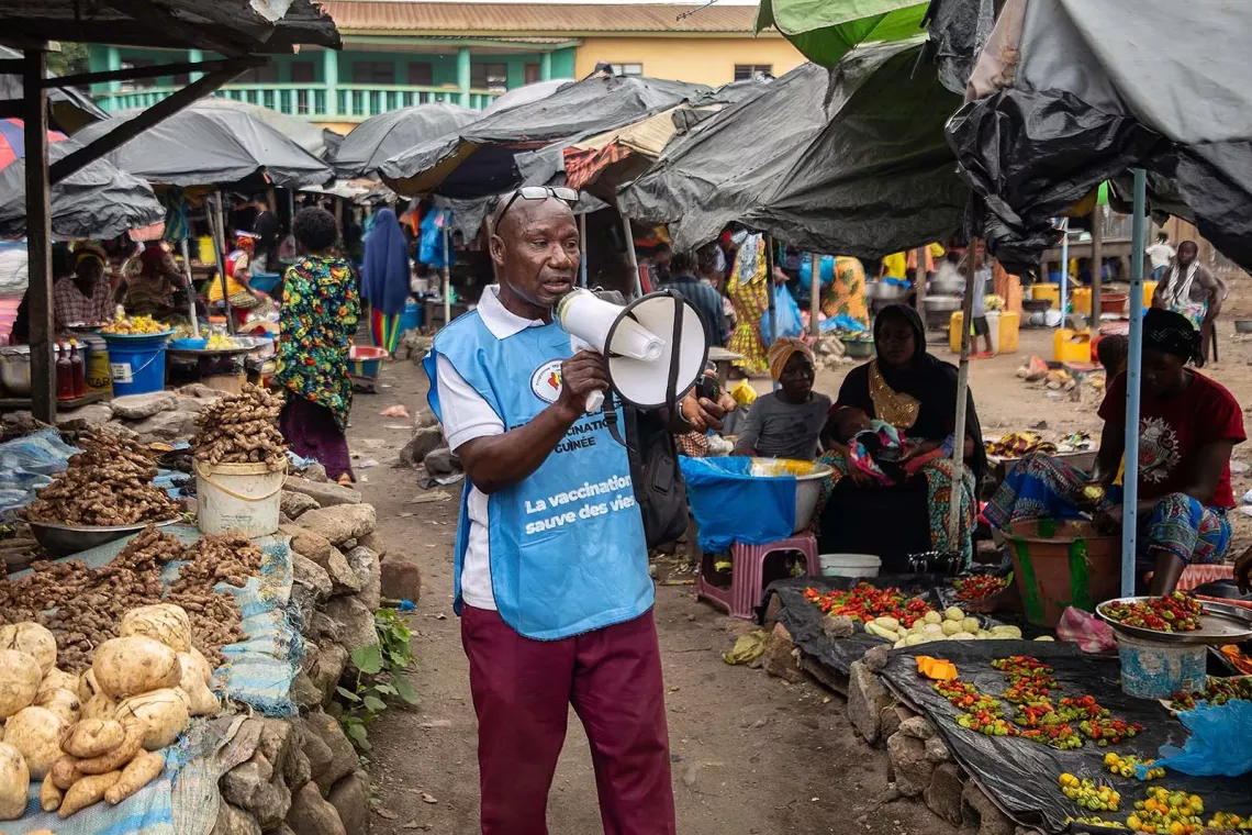 Man speaking into a megaphone at a street food market. 