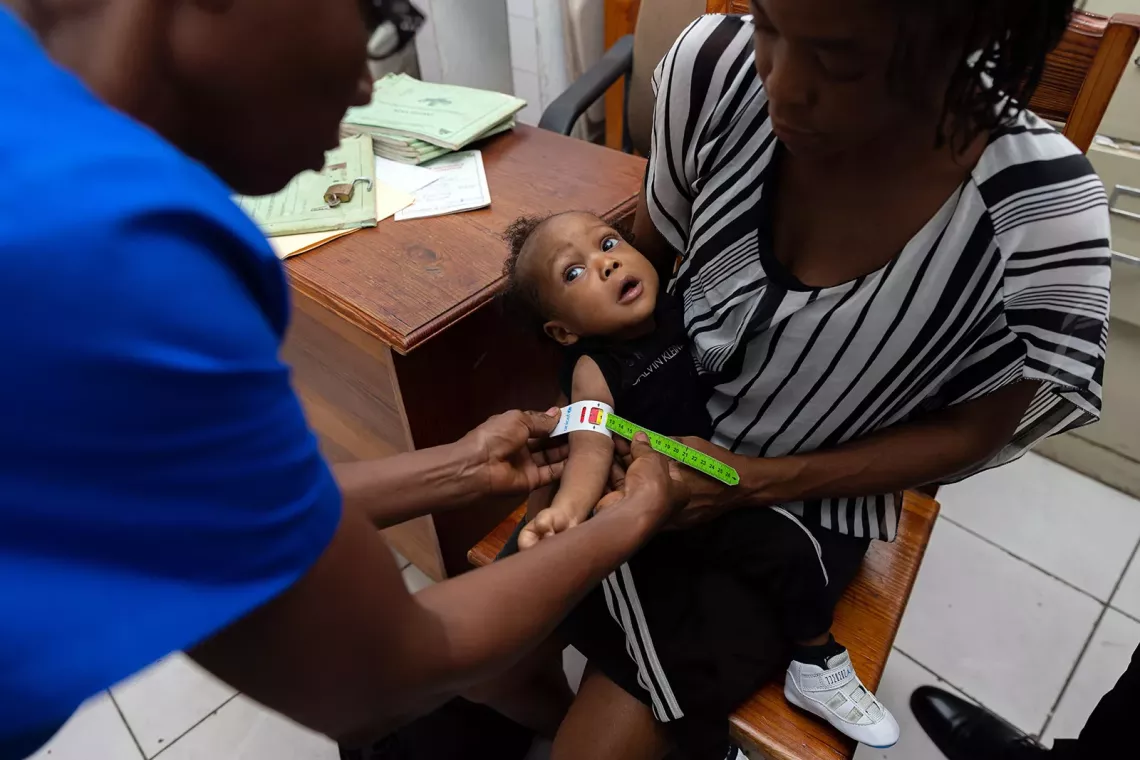 Mid-upper circumference tape is used on a baby as her mother holds her.