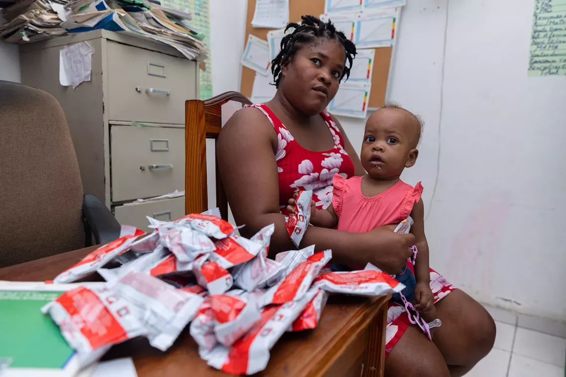 A mother and her daughter sit in a doctor's office with ready-to-use therapeutic food on the table.