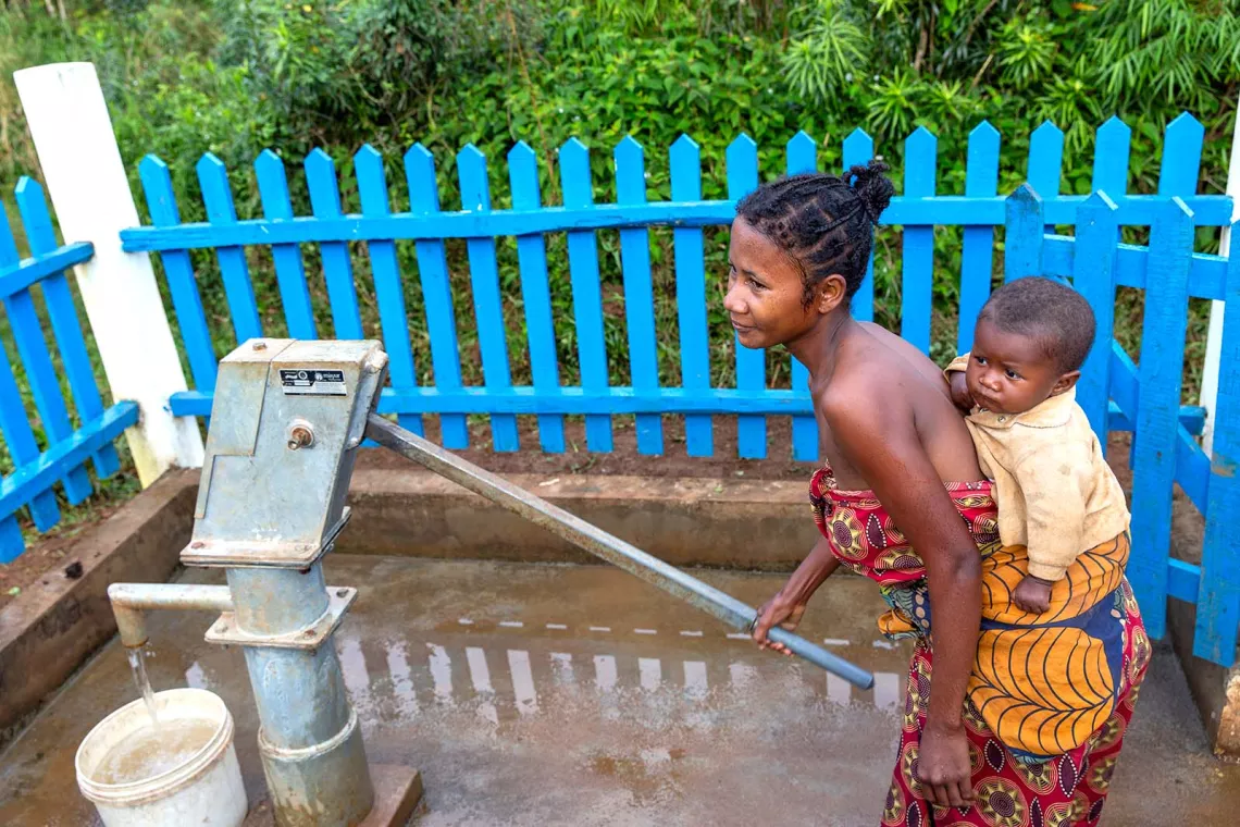 Woman holding a baby on her back collects water with a manual water from a borehole.