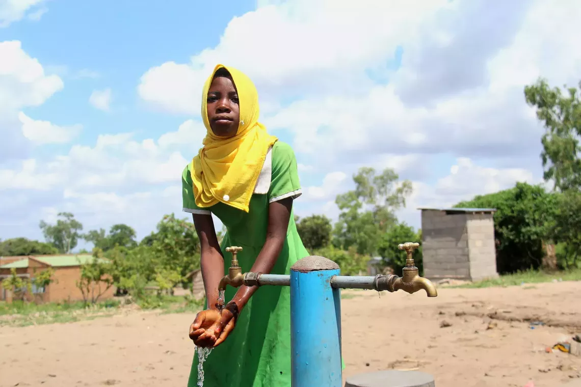 A teenage girl washes her hands at an outdoor tap. 