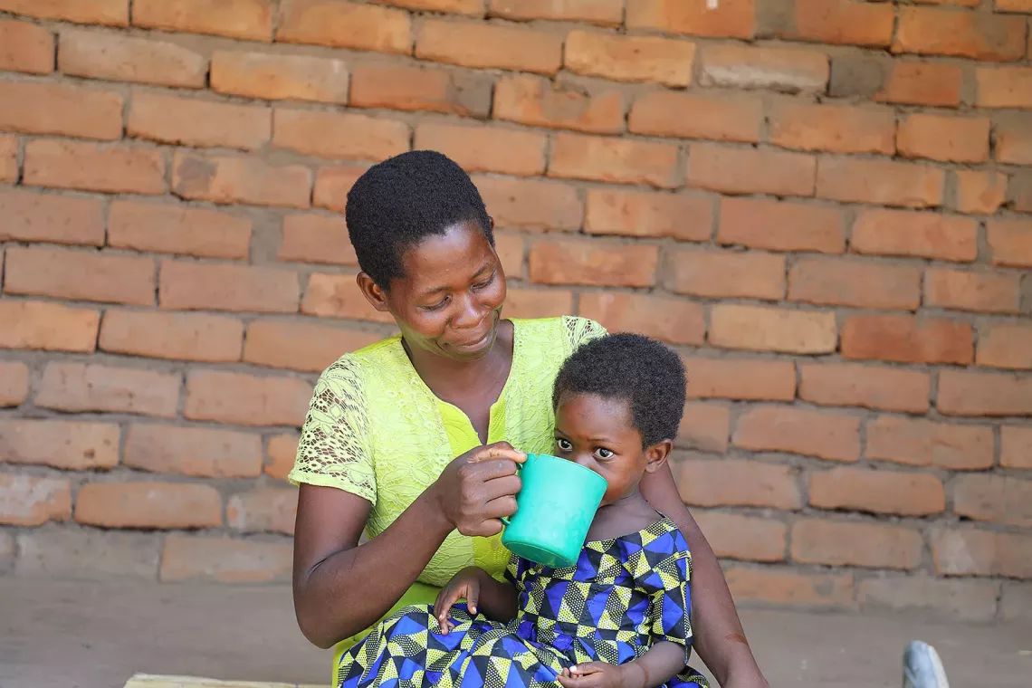 A woman gives water to a child sitting on her lap. 