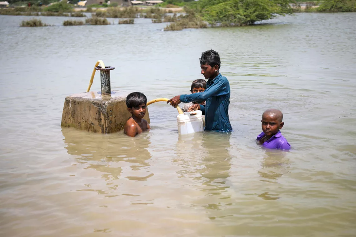Four young boys are collecting drinking water standing in the flood water