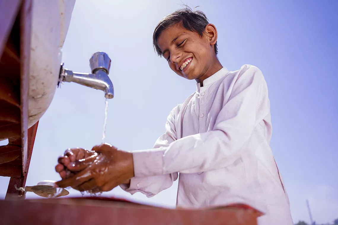 A boy smiles while washes his hands at a handwashing station set up by UNICEF in Pakistan.