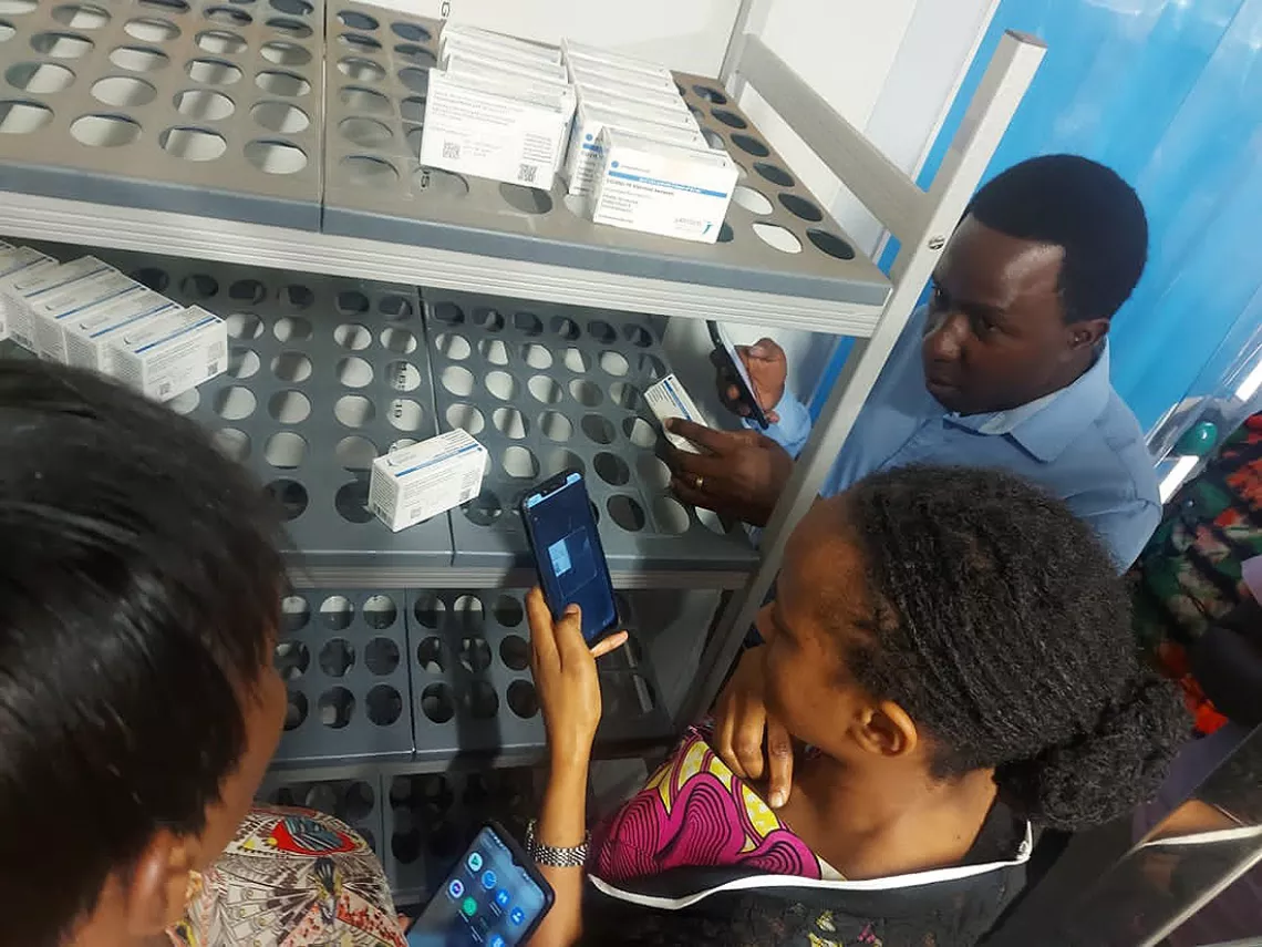 A woman, watched by a man and another woman, scans the barcode of a medicine in Rwanda.