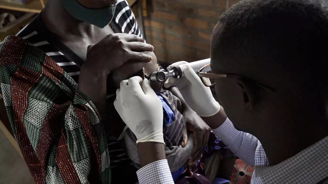 A young child in her mother's arms is fitted for hearing aids.