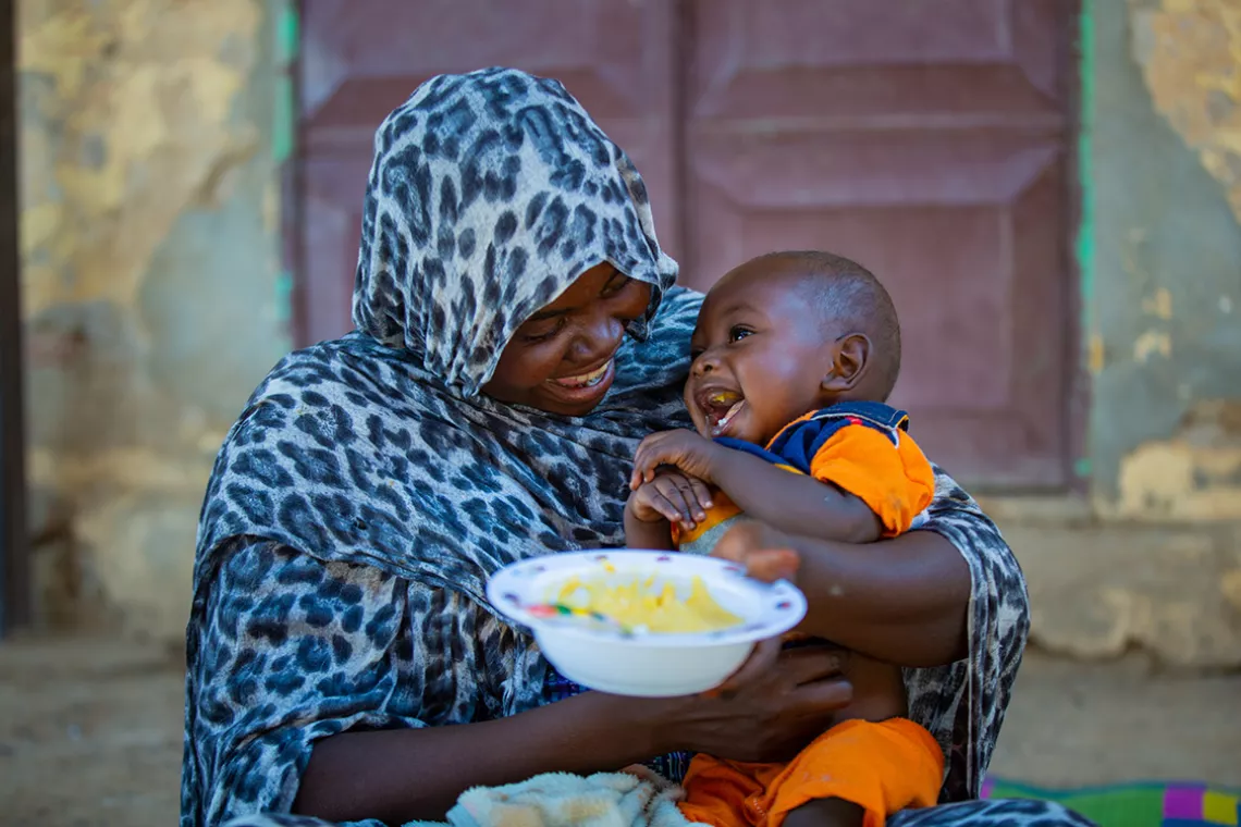 Mother feeding her child with the complementary food bowl. 