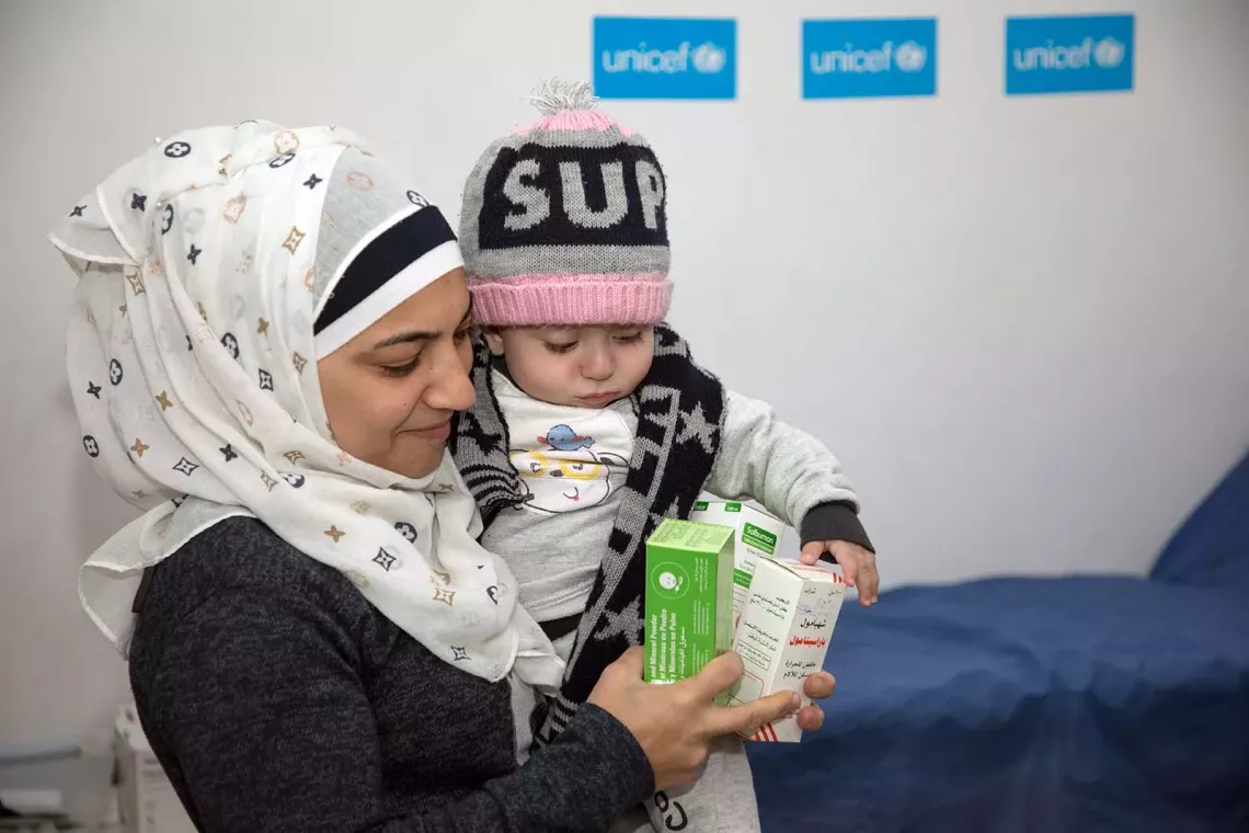 A woman holds a baby with her left hand while has her right hand full with packages of medicines. 