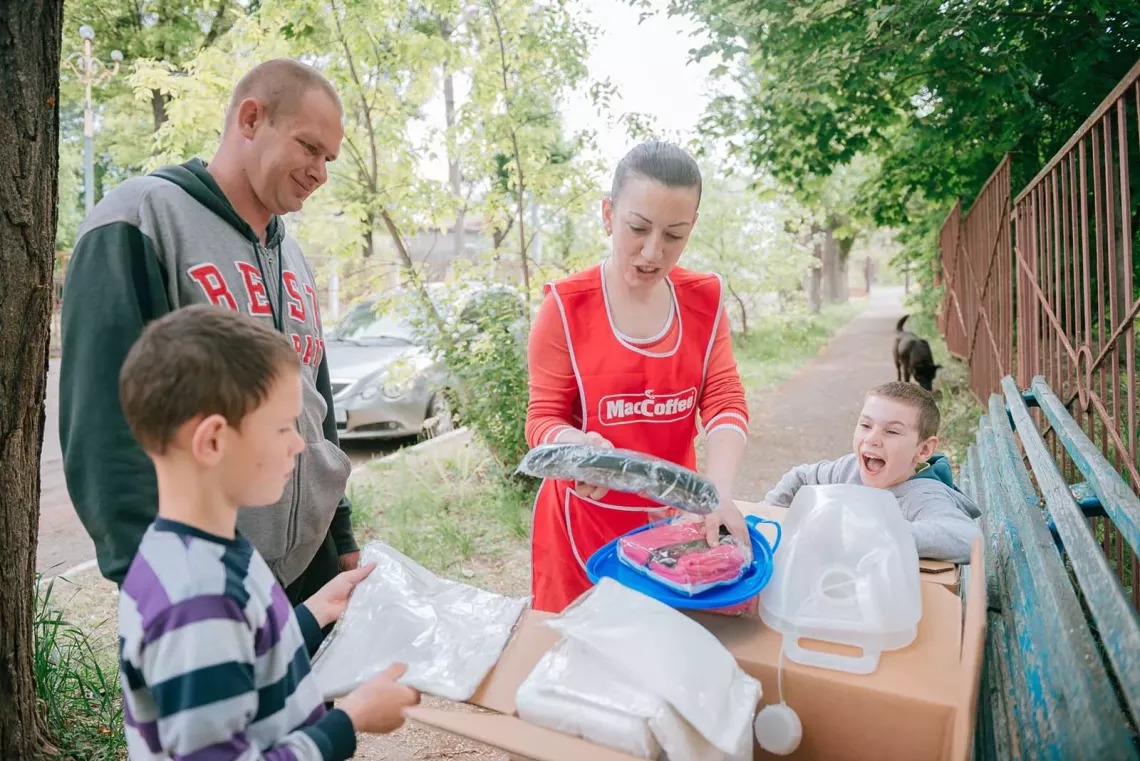 A woman surrounded by two children and a man unpack a WASH and Dignity Kit they received from UNICEF.
