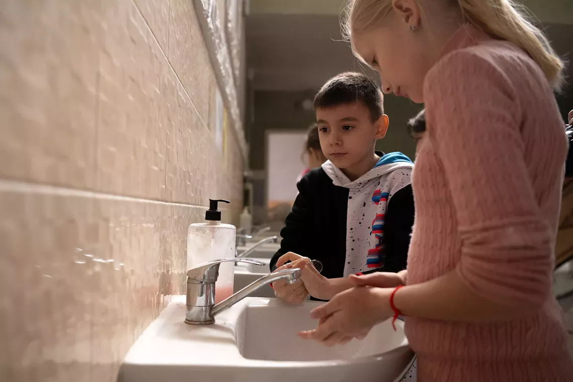 Two children by a small sink washing their hands. 