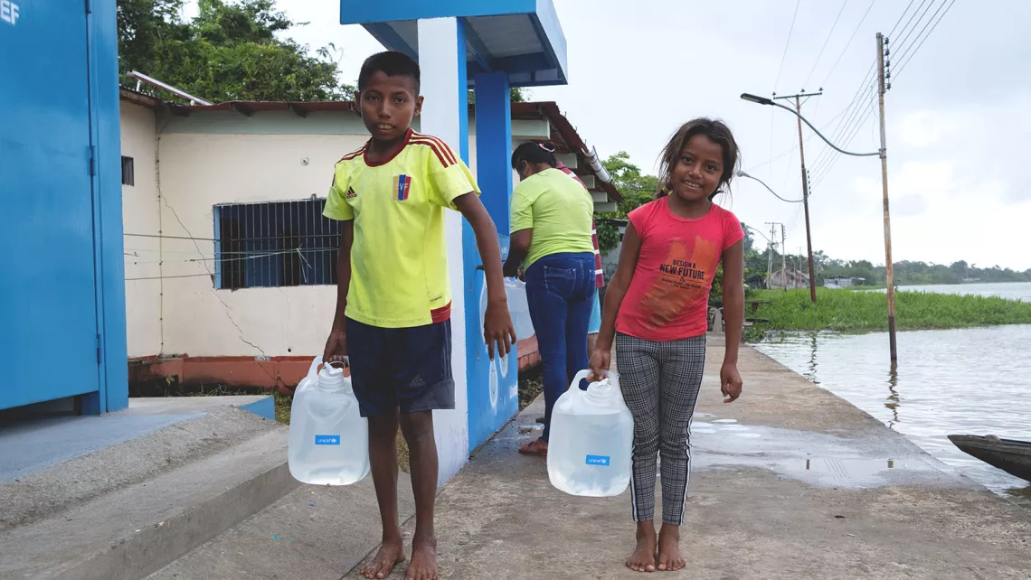 A boy and a girl carry jerry cams they used to carry water they fetched from a solar-powered water treatment plant.