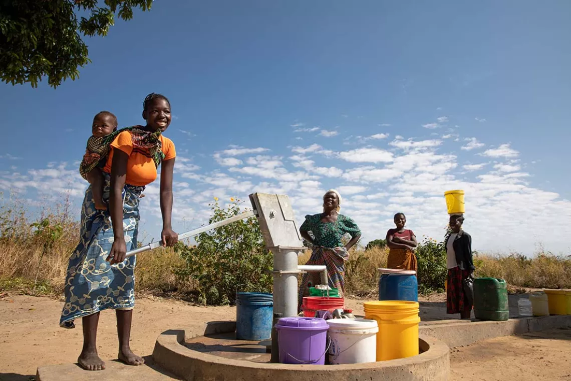 With her baby on her back, Edna Njambe collects water from a handpump while other women wait for their turn. 