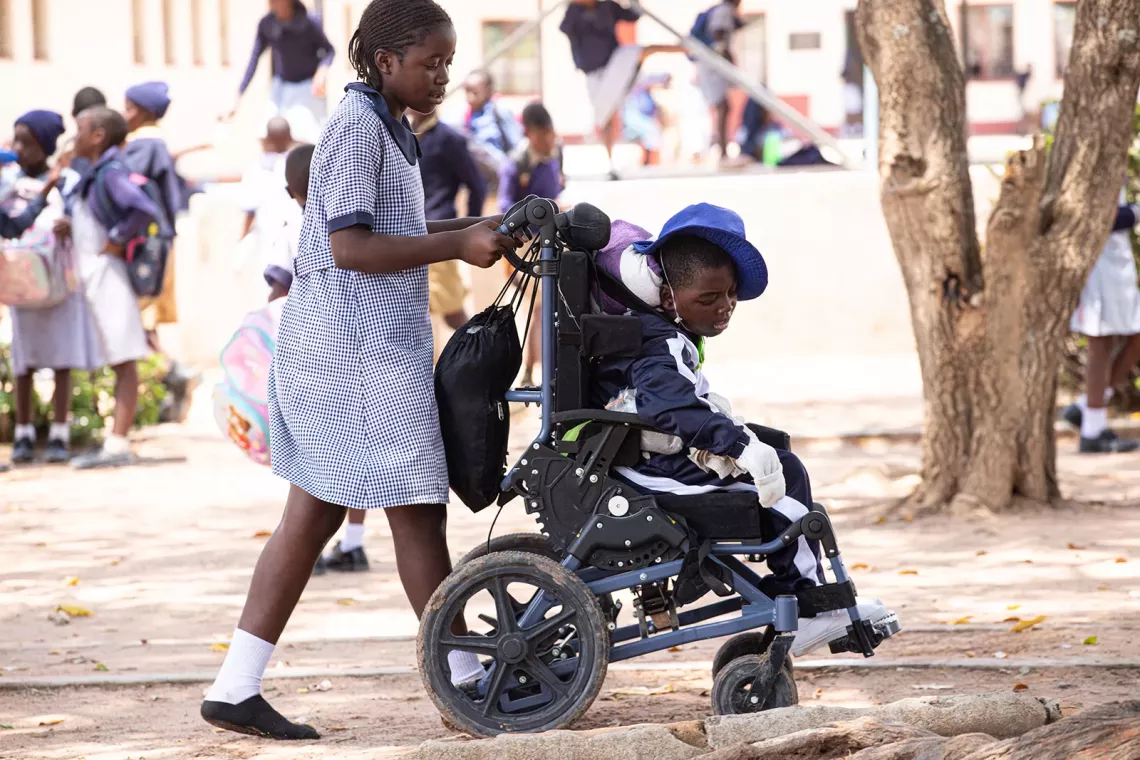 Student in a wheelchair is wheeled around by one of her classmates. 