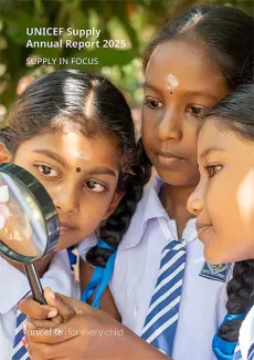 Three girls in school uniform examine a flower with a magnifying glass.