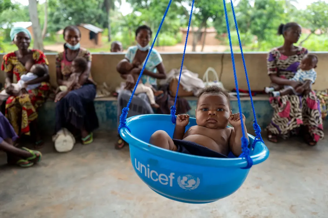 A child in blue plastic tub with the UNICEF logo on is being weighed.