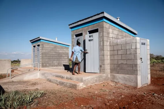 A person standing outside a small building is about to open its door where it reads WC.