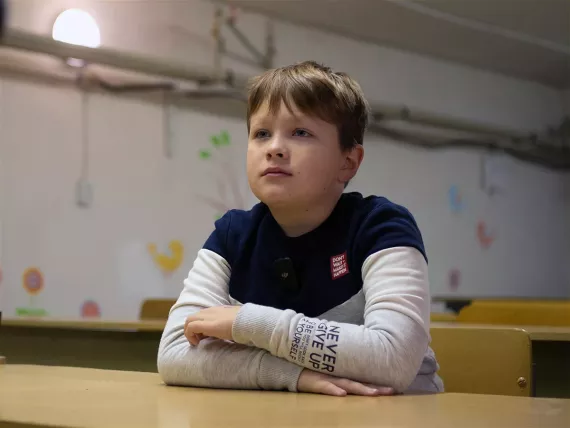  A boy with folded arms and sitting at desk in a classroom.