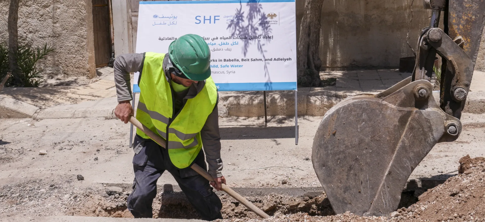 Worker Rida, wearing a yellow reflected vest and a green hardhat, excavates the ground to reach damaged water pipes.