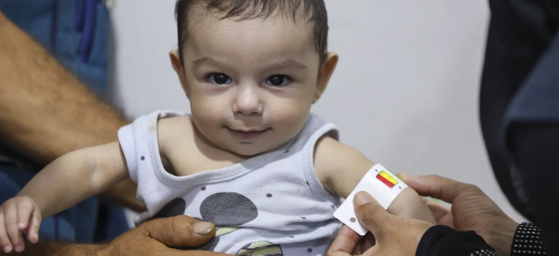 A baby boy has his mid-upper arm circumference being measured.