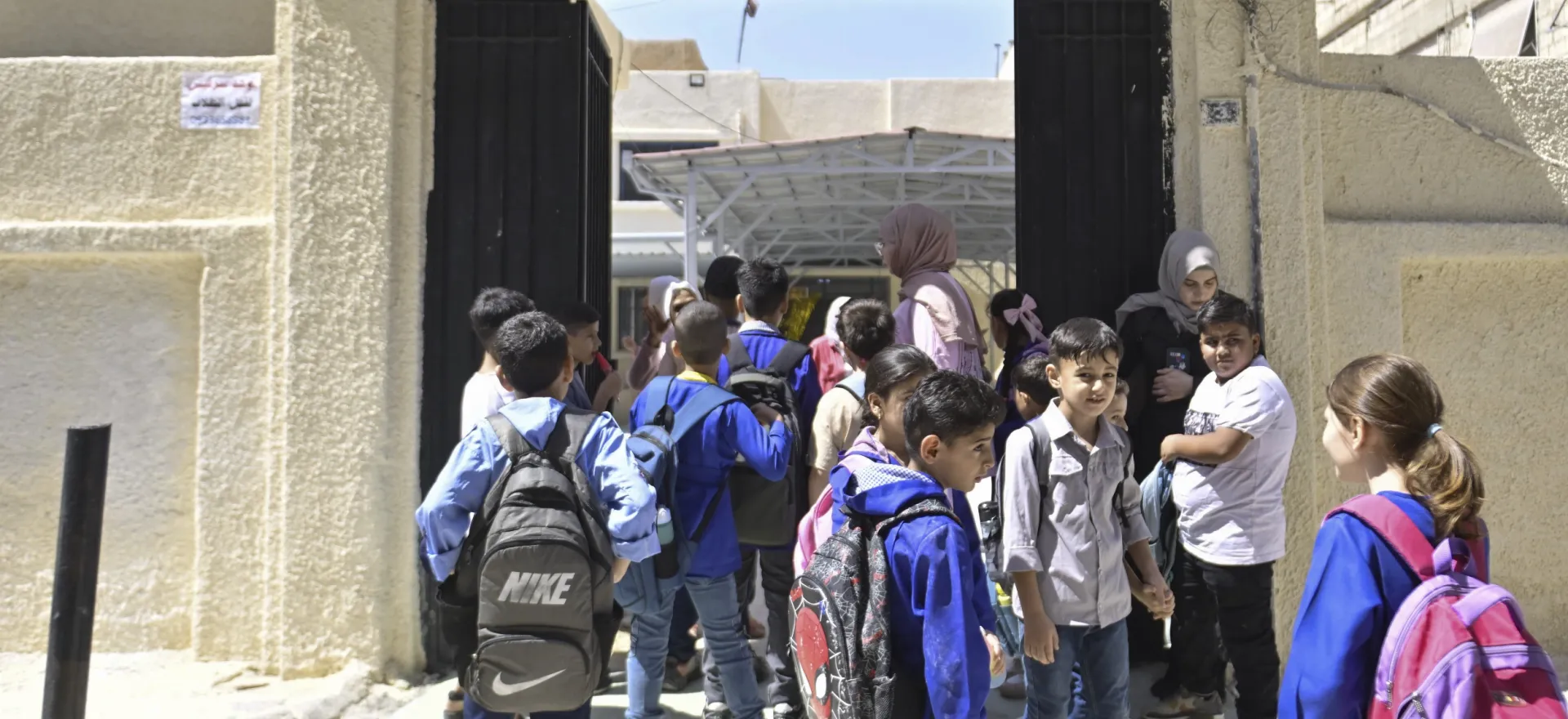 Children wearing school uniforms walk through a large entrance in a wall.