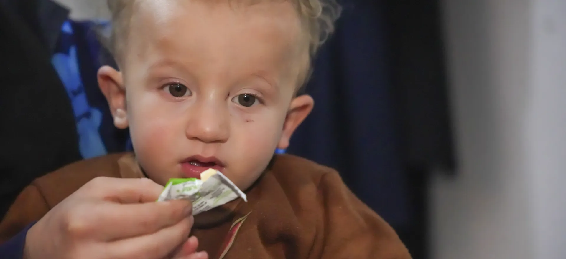 Abdulrahman, a one-year-old boy, eats a fortified small-quantity lipid-based nutrient supplement from a packet.