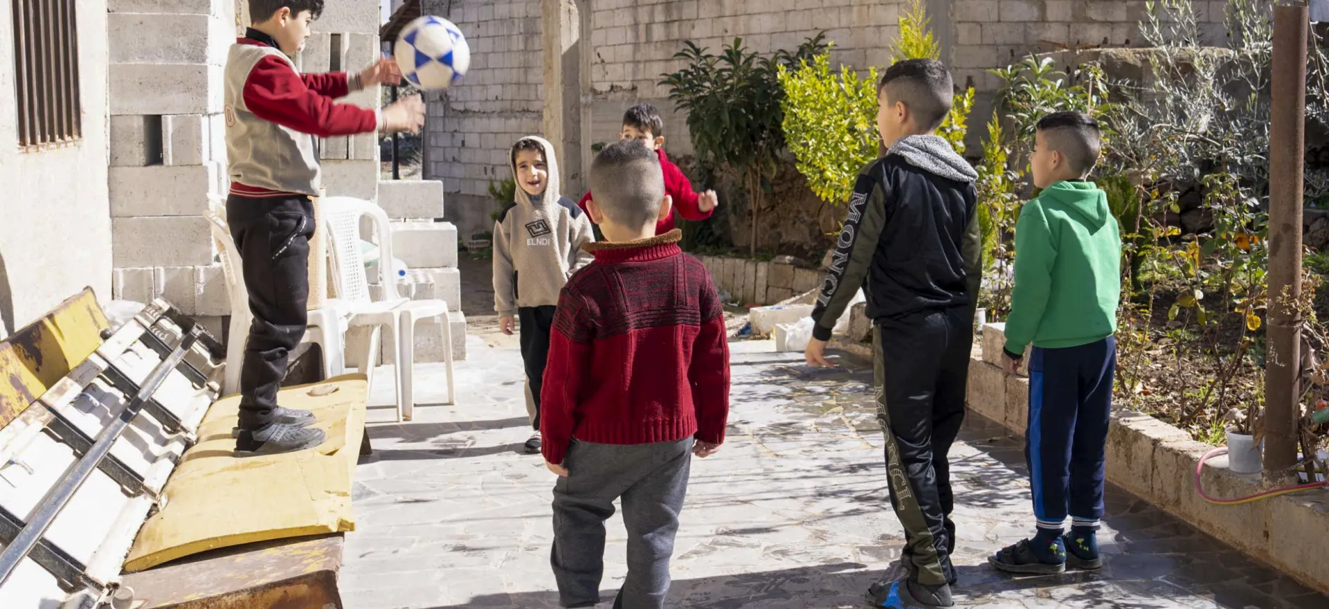 Children play outside their house with a ball.