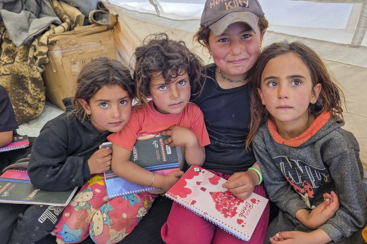 Three little girls sit huddled together inside a tent.