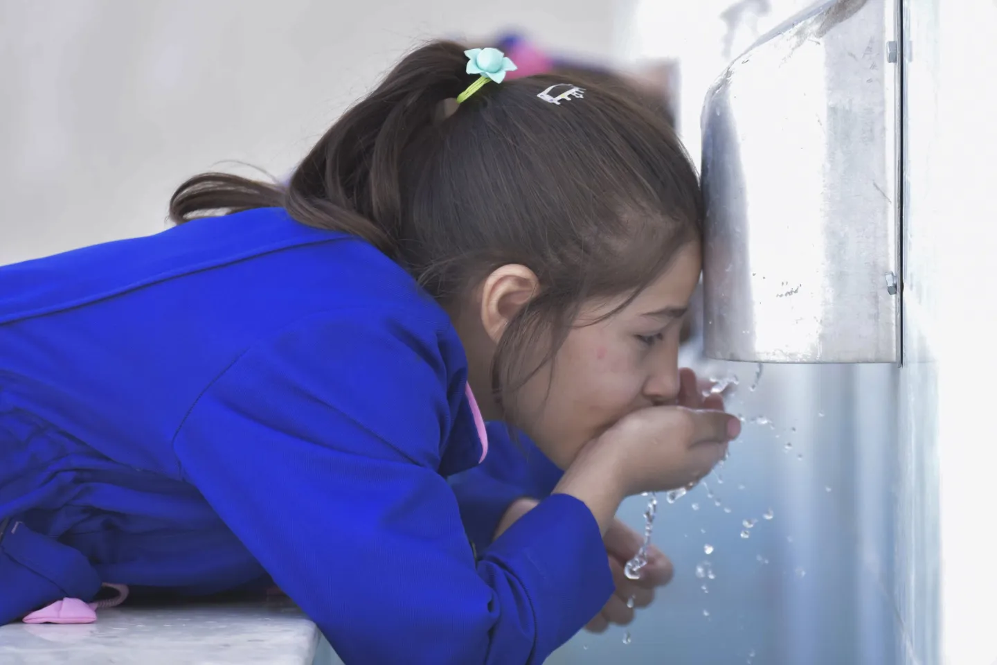A girl wearing a blue school uniform drinks water.