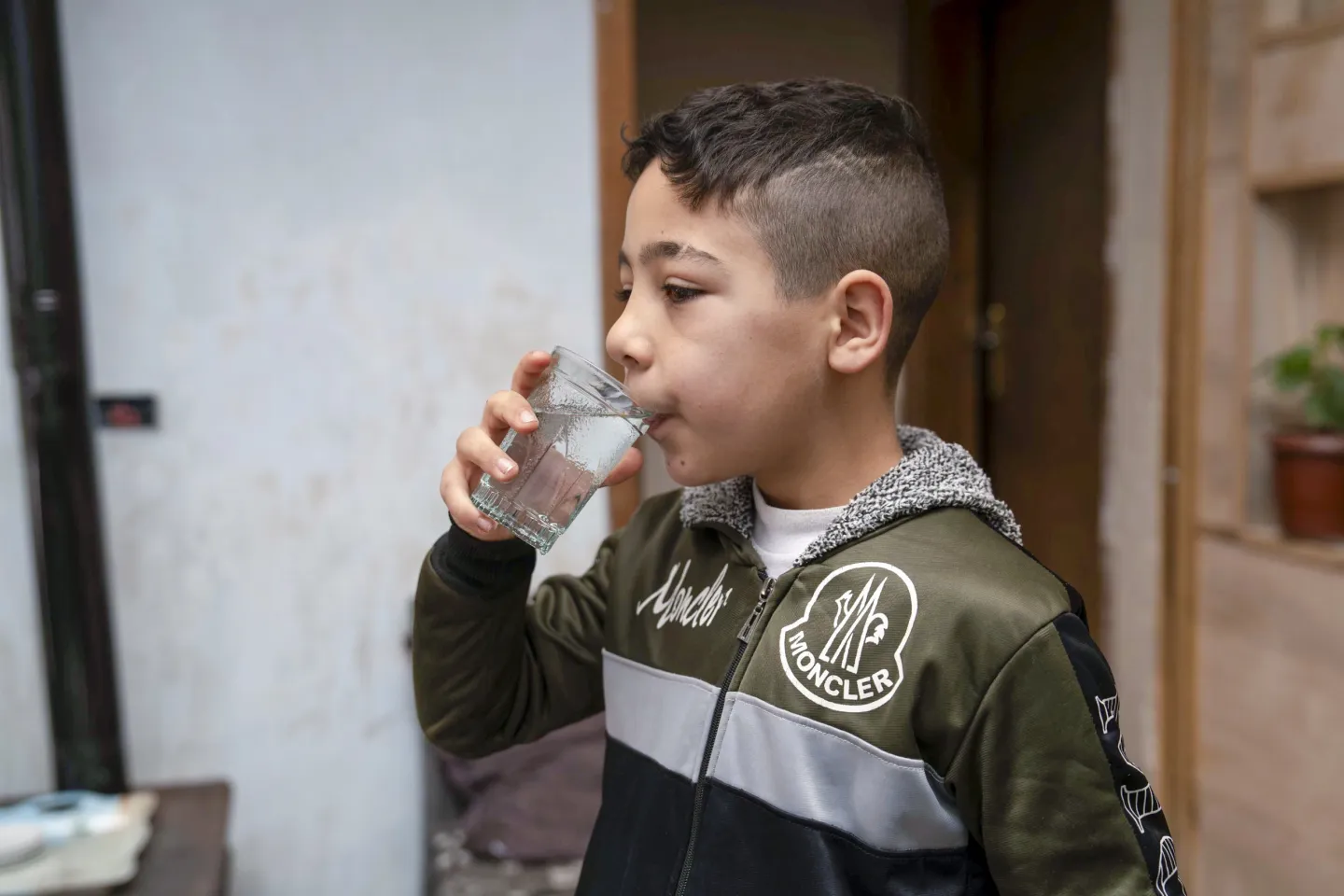 A young boy drinks water from a clear glass.