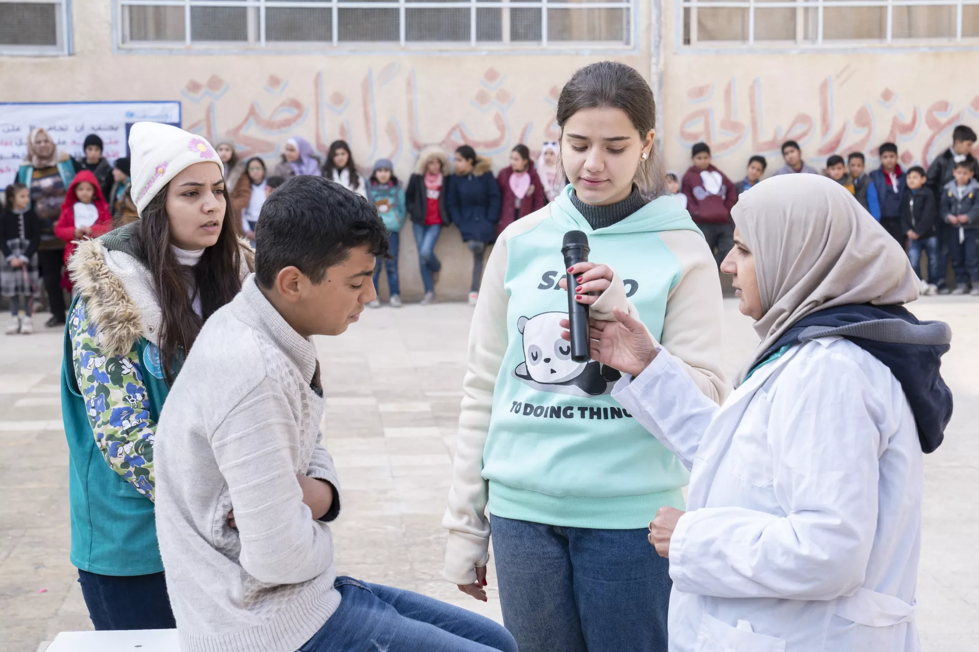 Girl speaking on microphone with two young people and a facilitator looking on.