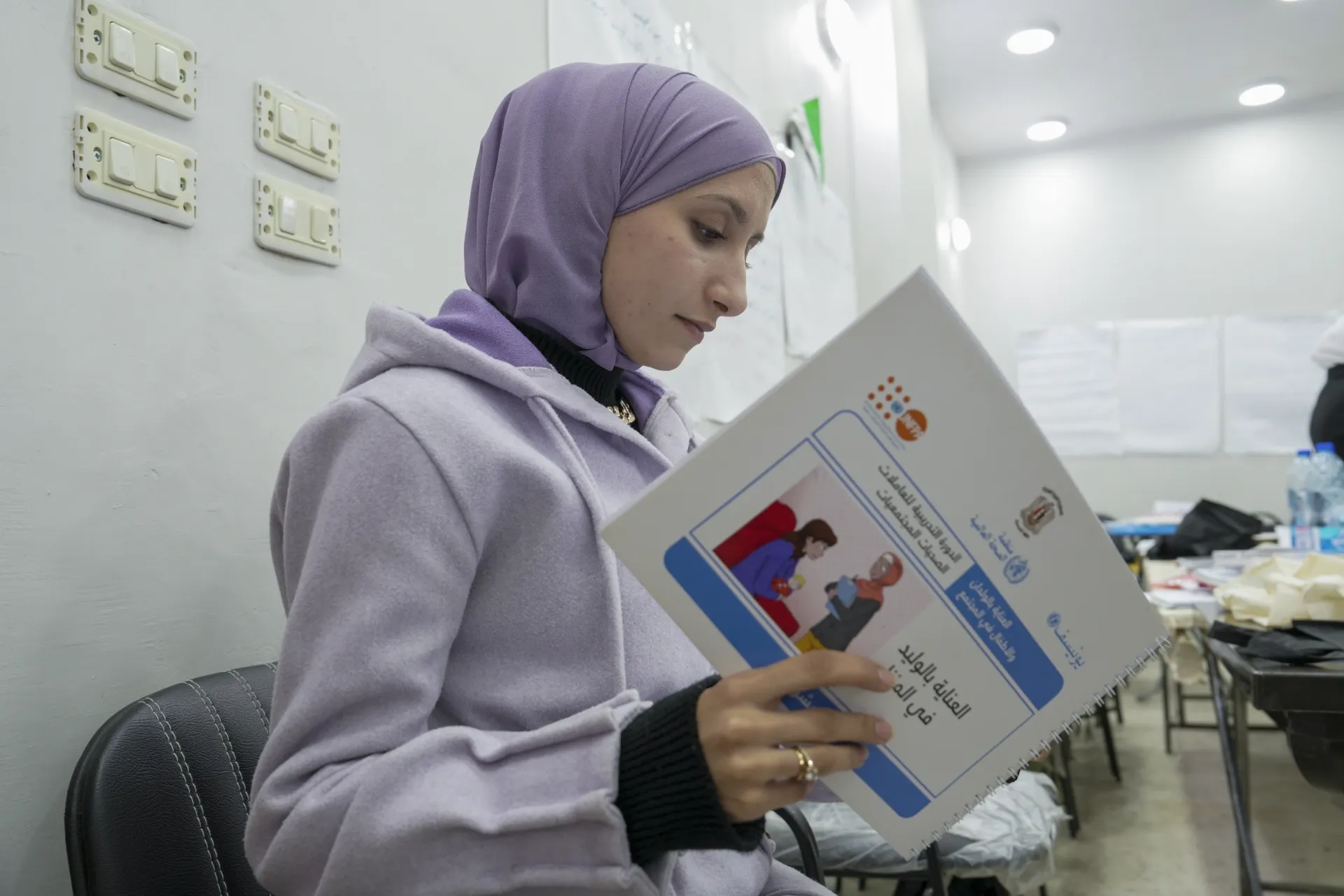 A woman wearing a lilac outfit reads a booklet with colourful pages.