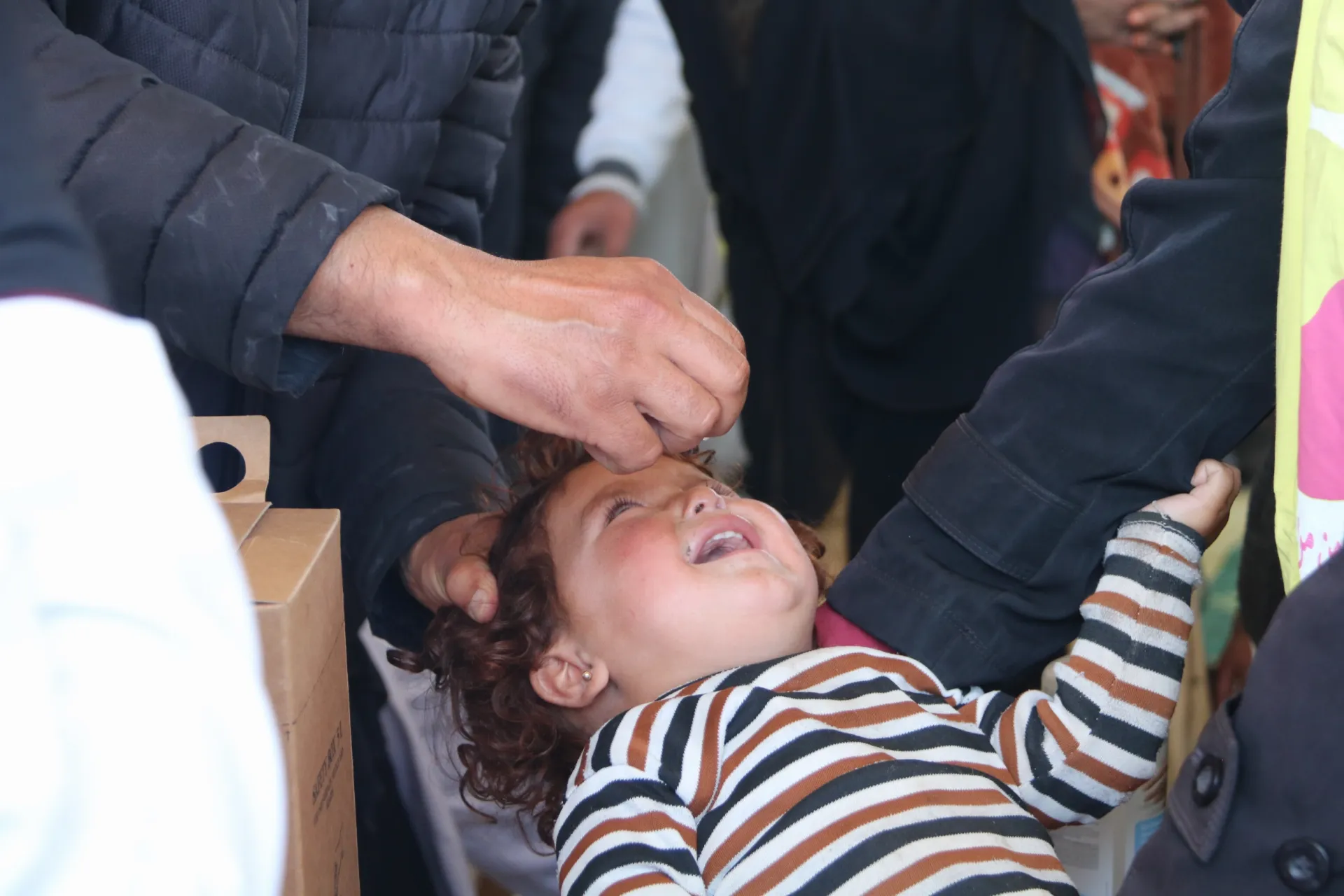 A vaccinator administers an oral vaccine to a child.