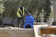 A worker wearing a yellow reflective vest bends down to inspect a large blue valve.