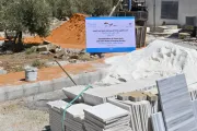 Construction materials are stacked up on a road, with a large signboard with a UNICEF and other logos on it.