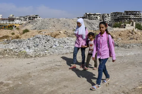 three sisters walking to school past rubble heap