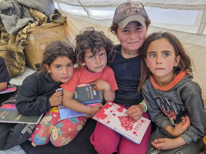 Three little girls sit huddled together inside a tent.