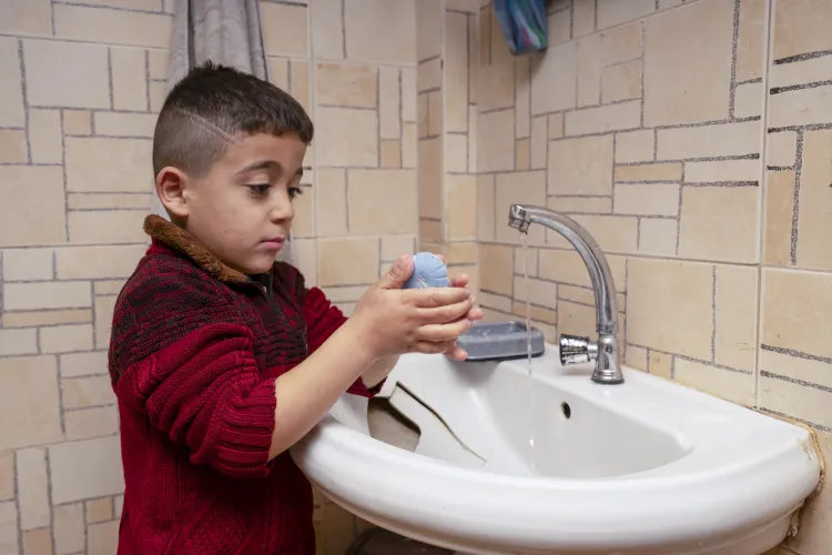 A young boy washes his hands with soap at a sink in his house.