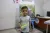 A young boy holding a box in his right hand stands in health centre.