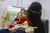 A girl wearing a red top looks up from where sits on her mother's lap, while her mid-upper arm circumference is measured.